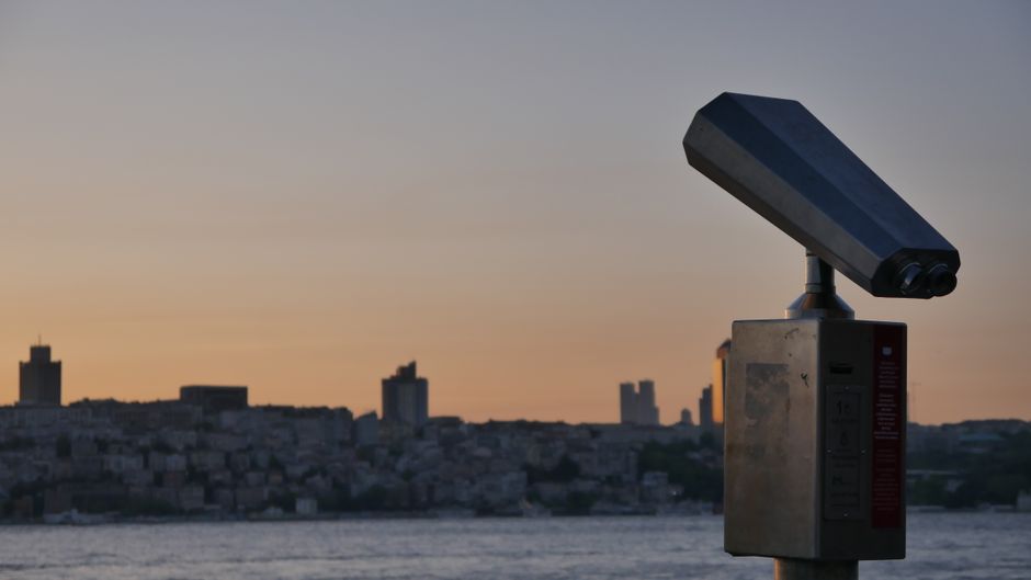 Binoculars overlooking the city skyline of Istanbul at sunset, with vibrant colors in the sky.